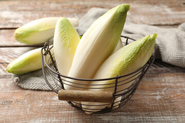 Fresh raw Belgian endives (chicory) in metal basket on wooden table