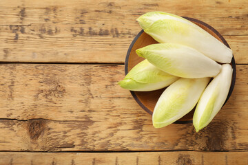 Fresh raw Belgian endives (chicory) in bowl on wooden table, top view. Space for text - obrazy, fototapety, plakaty
