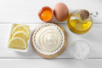 Fresh mayonnaise sauce in bowl and ingredients on white wooden table, flat lay