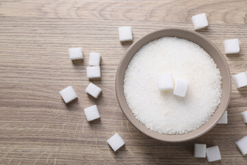 Different types of white sugar in bowl on wooden table, top view. Space for text