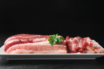 Pieces of raw pork belly and parsley on black textured table, closeup. Space for text