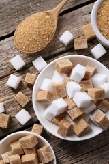 Different types of sugar in bowls and spoon on wooden table, flat lay