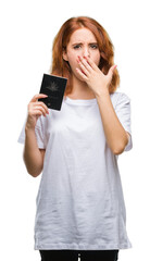 Fototapeta premium Young beautiful woman holding passport of australia over isolated background cover mouth with hand shocked with shame for mistake, expression of fear, scared in silence, secret concept