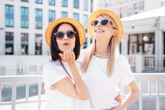 Two young beautiful smiling hipster female in trendy summer white t-shirt and jeans clothes. Carefree women posing in street. Positive models having fun. Cheerful and happy. In hat, sunglasses
