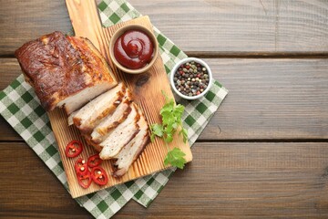 Pieces of baked pork belly served with sauce, chili pepper and parsley on wooden table, top view....