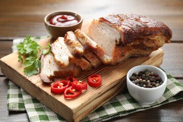 Pieces of baked pork belly served with sauce, chili pepper and parsley on wooden table, closeup