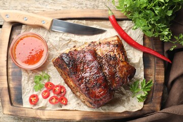 Piece of baked pork belly served with sauce and chili pepper on wooden table, top view