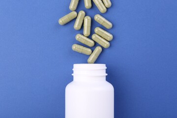 Bottle and vitamin capsules on blue background, top view