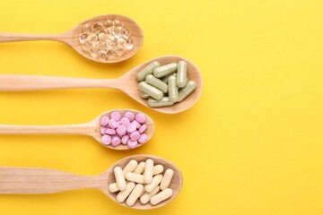 Different vitamin pills in wooden spoons on yellow background, flat lay. Space for text