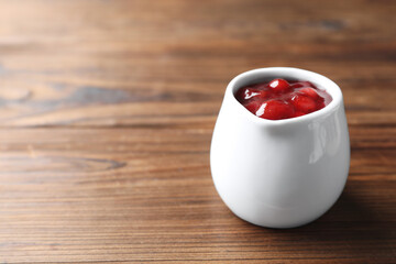 Fresh cranberry sauce in pitcher on wooden table, closeup. Space for text