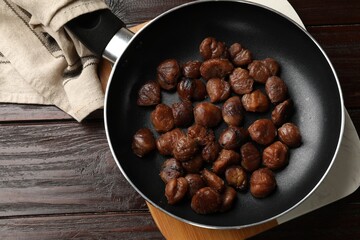 Roasted edible sweet chestnuts in frying pan on wooden table, top view