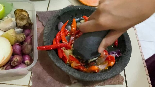a woman traditionally grinds chilies in a stone mortar to make chili sauce