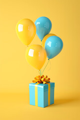 Festive Gift Box with Floating Balloons. A cheerful yellow and blue gift box tied with a ribbon, adorned with floating balloons on a yellow background. Vertical photo