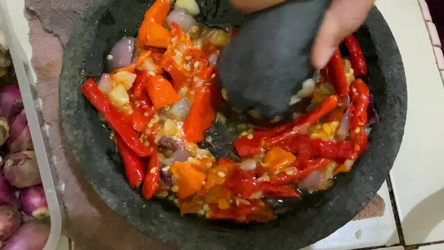 a woman traditionally grinds chilies in a stone mortar to make chili sauce