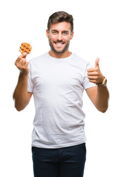 Young handsome man eating a sweet waffle over isolated background happy with big smile doing ok sign, thumb up with fingers, excellent sign