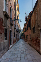 Fototapeta na wymiar Lonely path way along the Venetian city with high facades and mystic shadows