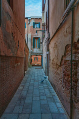 Lonely path way along the Venetian city with high facades and mystic shadows