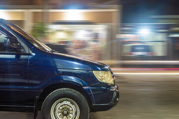 panning photography of a dark blue minibus driving fast at night in an urban area with shops