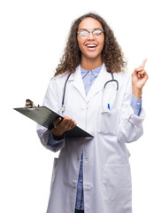 Young hispanic doctor woman holding a clipboard very happy pointing with hand and finger to the side