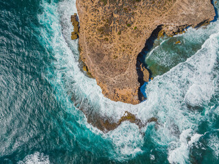 Aerial view of waves crashing against eroded cliffs along a rugged coastline