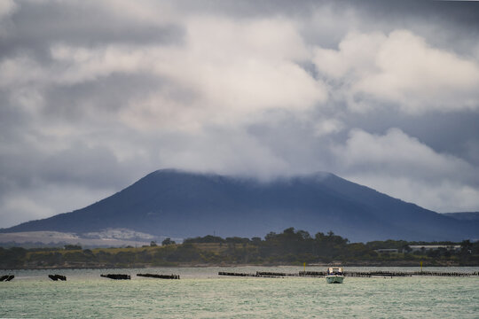 Distant view of a small boat anchored in front of a dark mountain shrouded in dramatic clouds