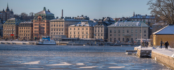 The old town Gamla Stan, piers and inner harbor ferry Djurgården at the icy bay Strömmen, a sunny winter day in Stockholm