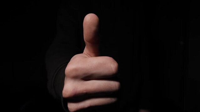 Close-up of a man's hand showing a thumbs up gesture on a black background.