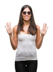 Young beautiful hispanic wearing sunglasses showing and pointing up with fingers number ten while smiling confident and happy.