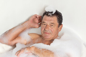 Mature man takes a bath with foam, home spa treatment.