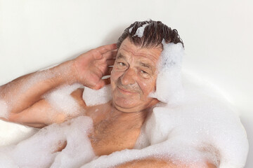 Mature man takes a bath with foam, home spa treatment.