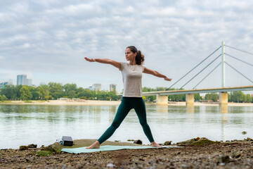 Fototapeta na wymiar A young and beautiful girl practicing yoga exercises by the river in the early morning.