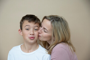 cool young teenager boy with white t-shirt posing together with his beautiful mother in front of brown background