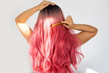 Rear view of a young beautiful woman with long pink curly hair combing her hair in the morning. Hair care concept.