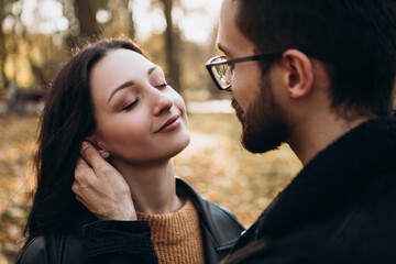 Heterosexual caucasian young loving couple walking outside in the city park in sunny weather, hugging smiling kissing laughing spending time together. Autumn, fall season, orange yellow red maple leav