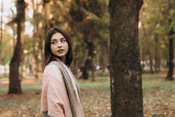 Caucasian woman walking outdoor smiling, portrait of young european lady in warm sunny autumn park season, fall, yellow orange red maple leaves, dressed warm coat and scarf

