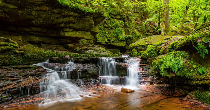 Panoramic view of Monbach creek valley with cascade near Bad Liebenzell in Black Forest, Germany. Blurred brook water motion with longtime exposure in an idyllic natural reserve after summer rainfall.