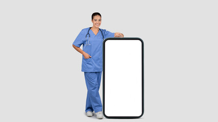 Smiling european millennial doctor nurse in blue uniform with big smartphone