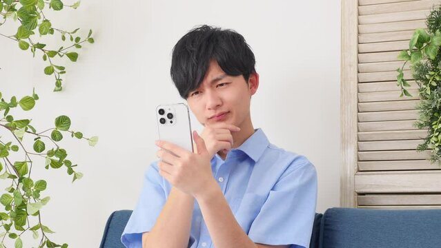 自宅で考えながらスマートフォンを使う男性