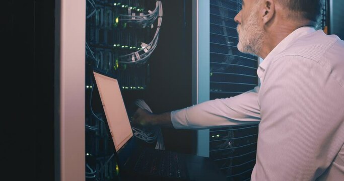Mature man in datacenter with laptop, cable for network maintenance or engineer in digital storage for data update. Tech support, system administration or technician online in server room on computer