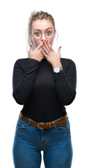 Young blonde woman wearing glasses over isolated background shocked covering mouth with hands for mistake. Secret concept.