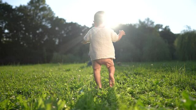 baby takes first steps in the park. happy family kid dream concept. dad teaches his son to walk takes the first steps in the park on lifestyle green grass. baby son taking first steps