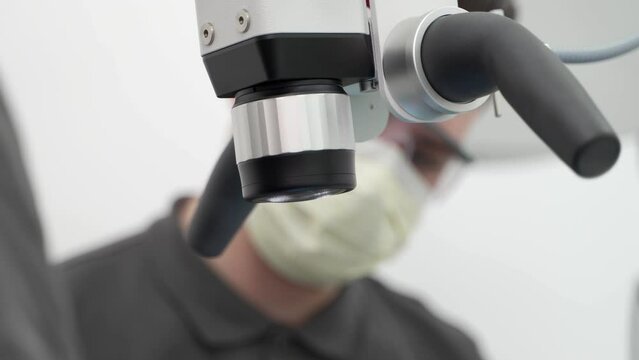 Close-up of male dentist with assistant patient using dental microscope during operation in the modern dental clinic. Endodontist, assistant treat root canals. Using microscope in dentistry.