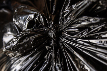 Detalhe de um nó em saco plástico preto com lixo, molhado, com gotas de água de chuva.