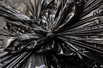 Detalhe de um nó em saco plástico preto com lixo, molhado, com gotas de água de chuva.