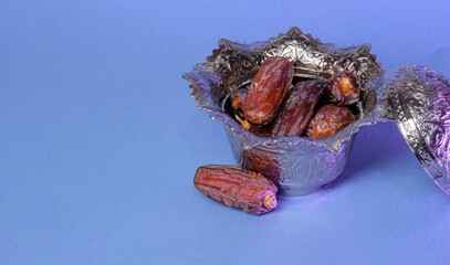 Dates in a silver sugar bowl on a blue background. Minimal visual for the concept of Ramadan.