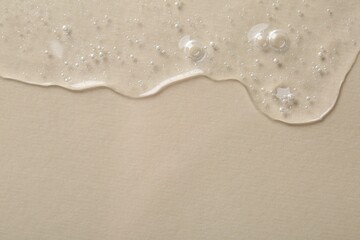 Clear cosmetic serum on beige background, macro view. Space for text