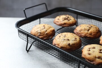 Cooling rack with delicious chocolate chip cookies on light grey table, closeup