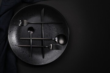 Stylish table setting. Plate, napkin and cutlery on black background, top view with space for text