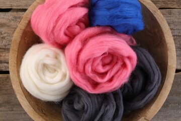 Fototapeta na wymiar Colorful felting wool in bowl on wooden table, top view