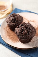 Delicious chocolate muffins and cacao powder on light grey table, closeup